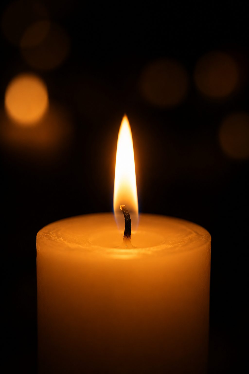 Close-up of a single lit candle against a dark background, symbolizing quiet remembrance